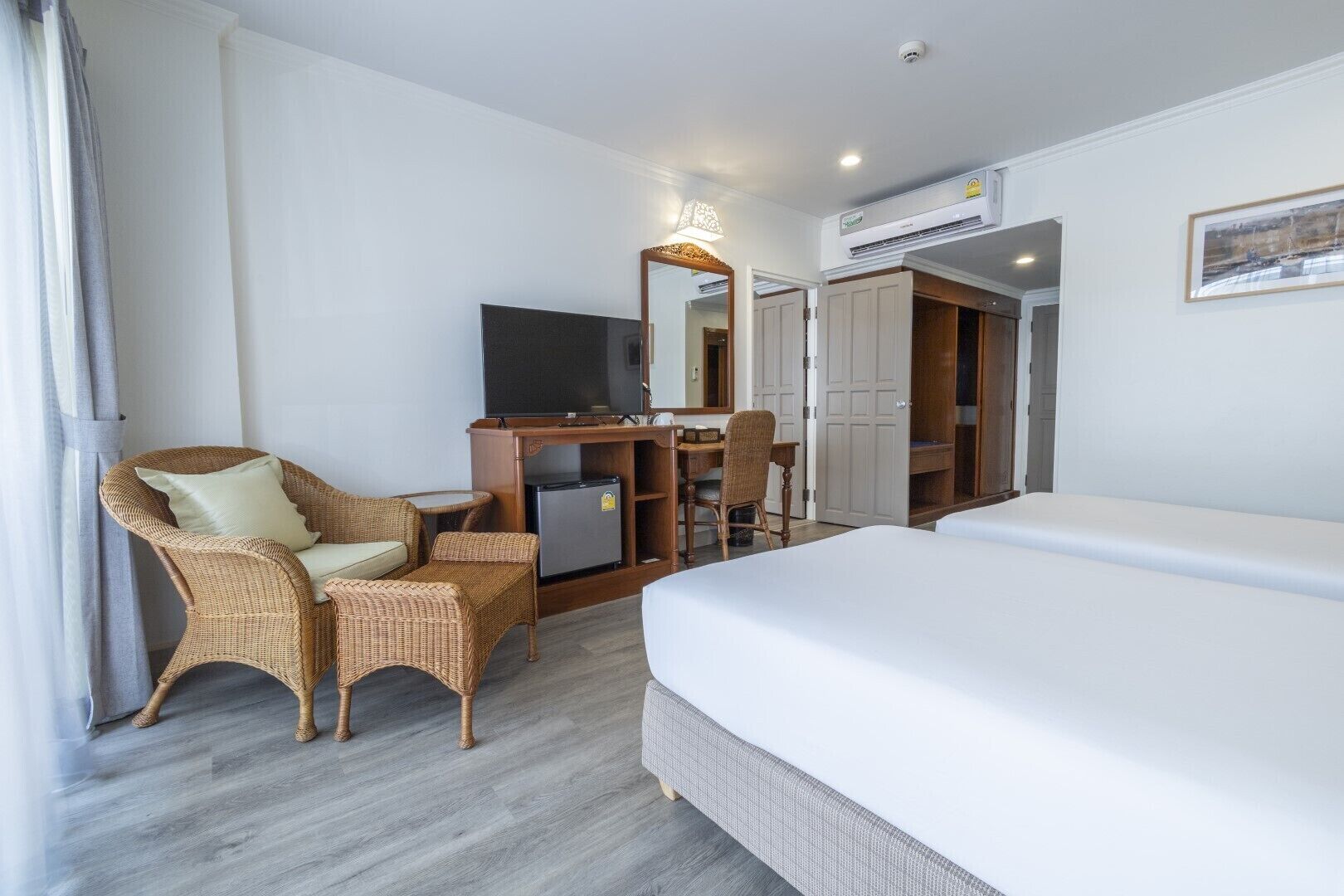 A hotel room with a bed, a desk with a computer, a chair, a wardrobe, and a television.