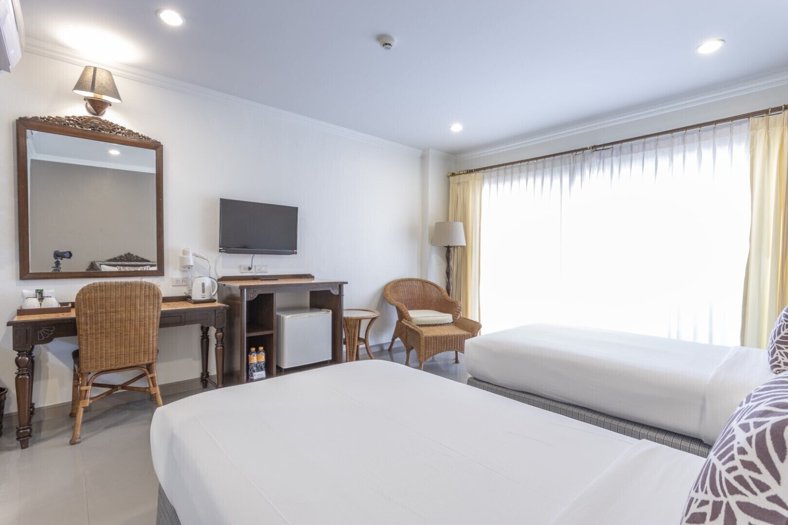 A hotel room with a bed, a desk with a computer, a chair, a television, and a window with curtains.