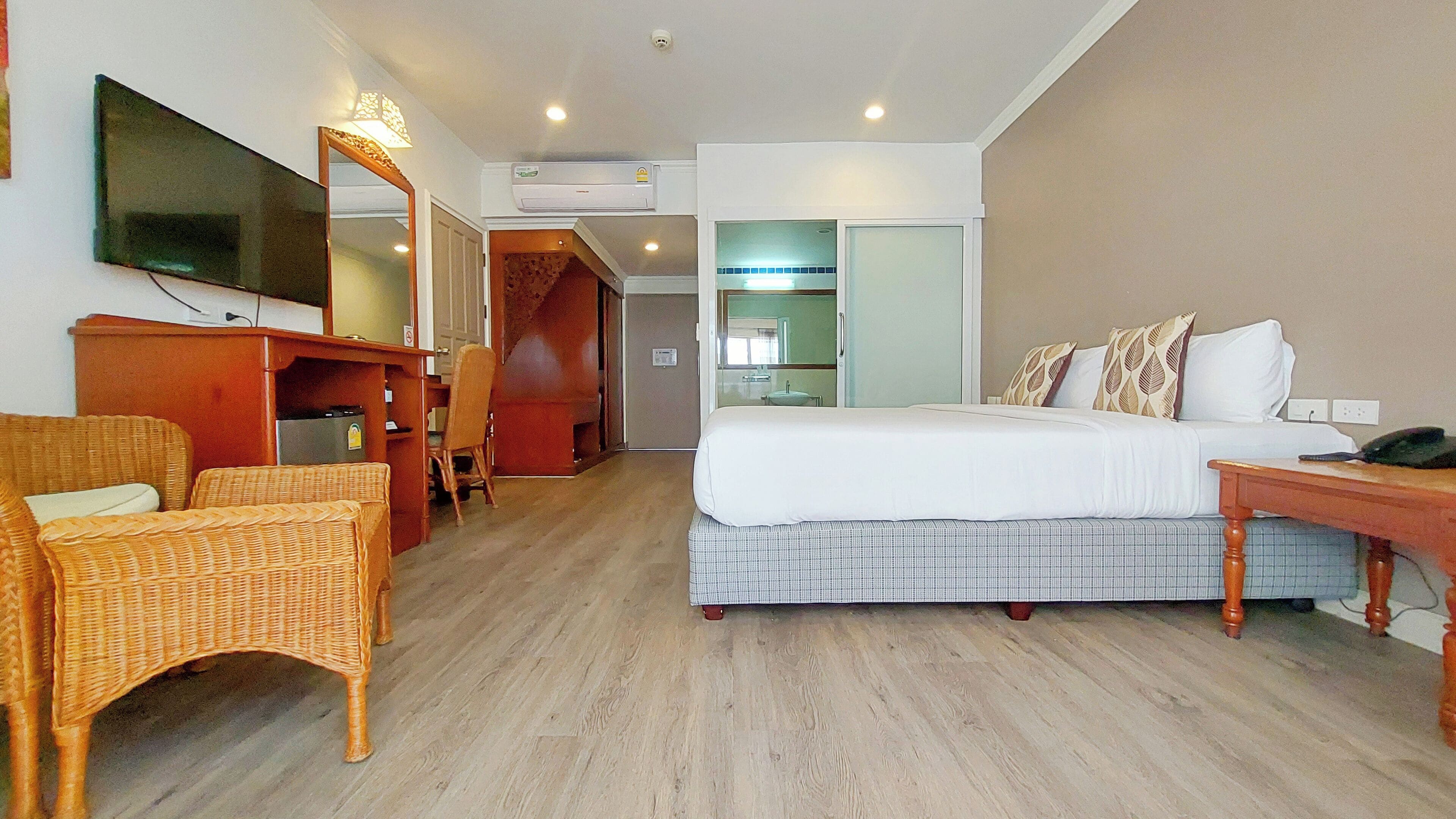 Habitación de hotel con cama, escritorio, silla, televisión y baño visible a través de una puerta abierta.