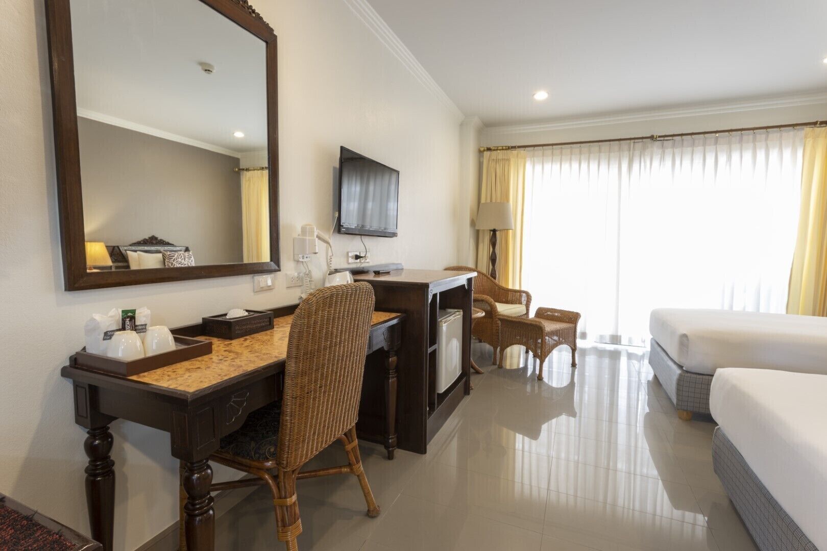 A hotel room with a bed, a desk with a chair, a television, and a large mirror.