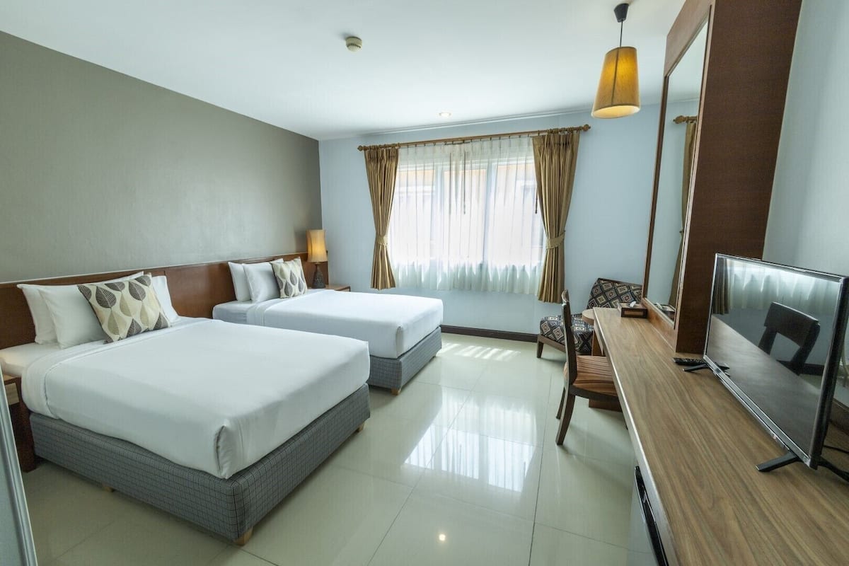 A hotel room with two beds, a TV, a desk, and a chair.