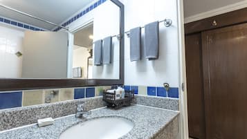 A bathroom with a granite countertop, a white sink, and a mirror. There are towels hanging on a rack and a wooden door.