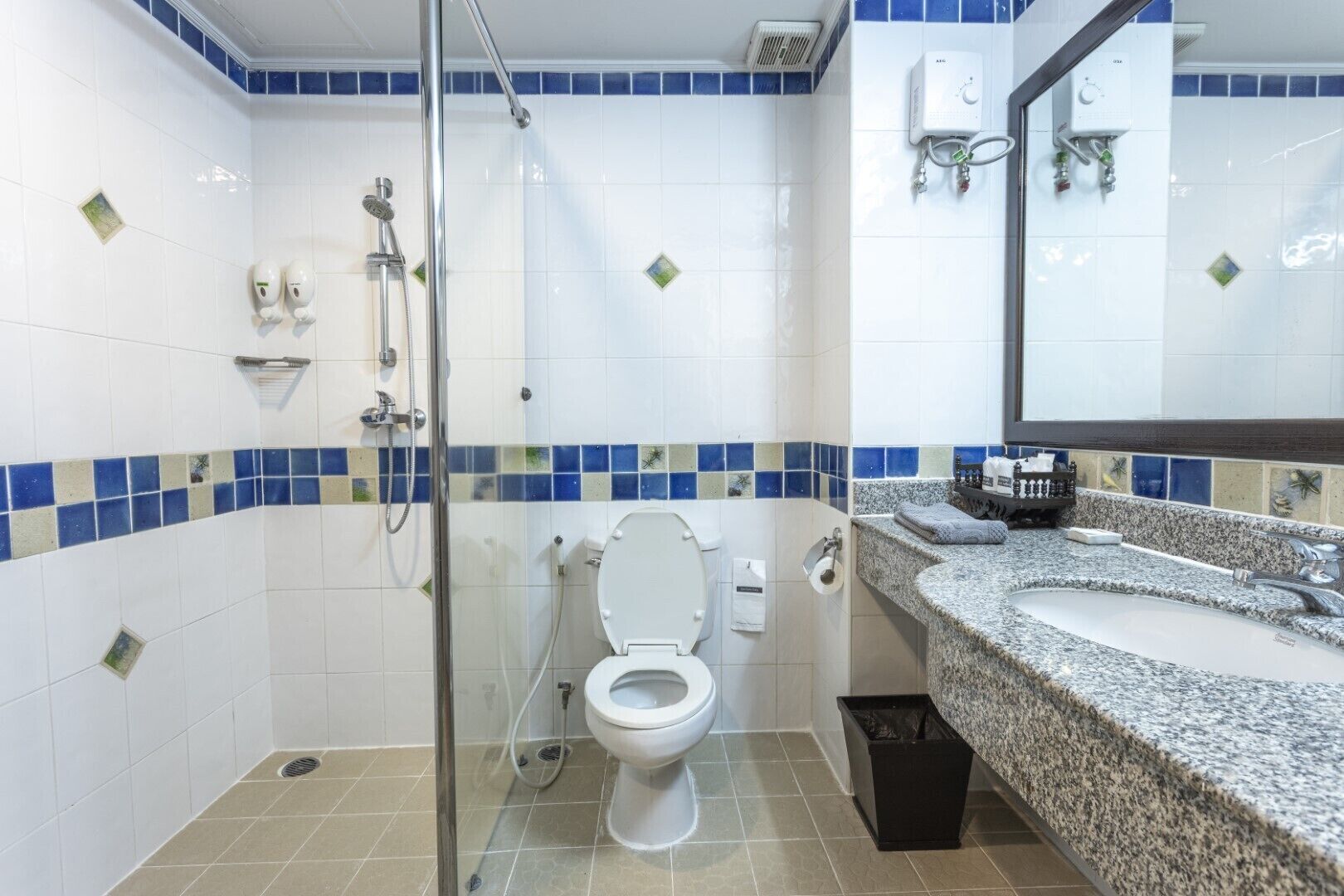 A bathroom with a glass-enclosed shower, a toilet, and a granite countertop sink.