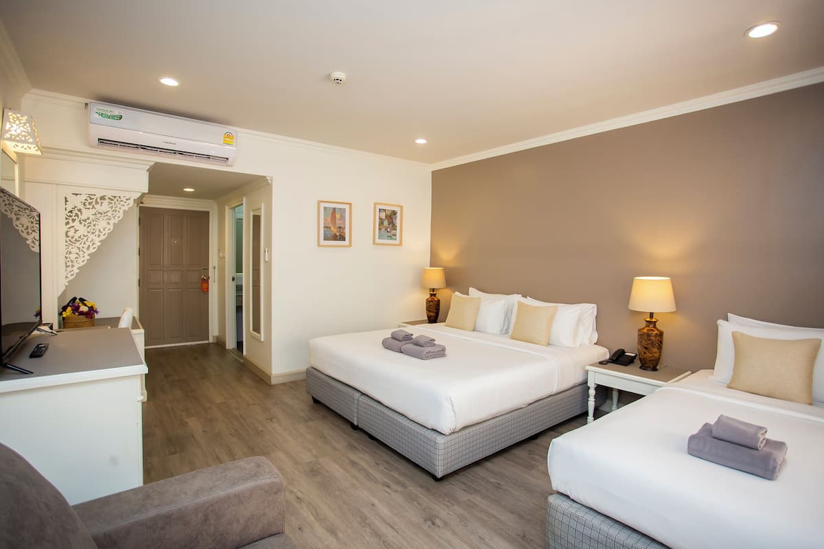 A hotel room with two beds, a desk, a chair, an air conditioning unit, and a door leading to another room.