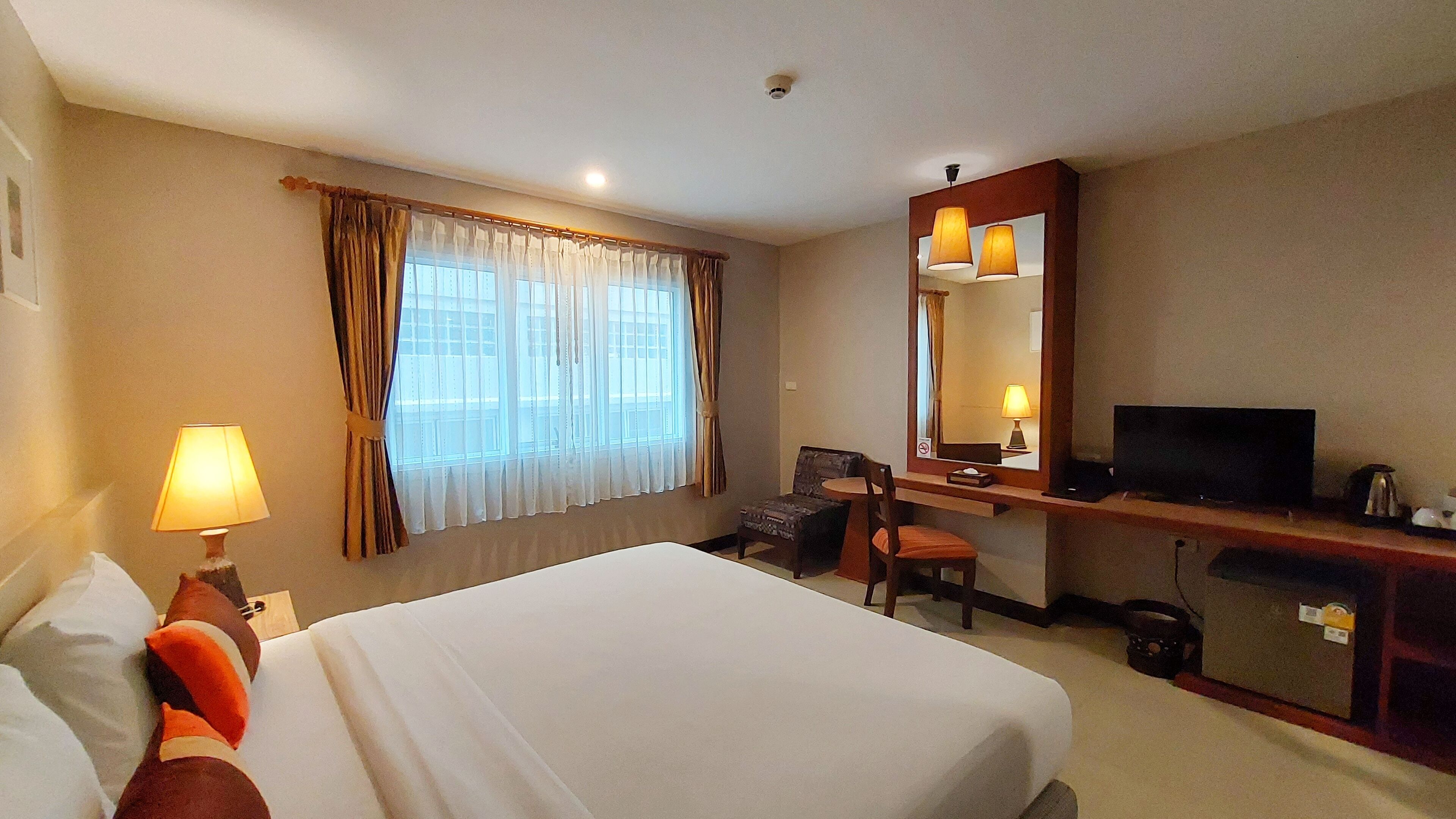 A hotel room with a bed, a desk with a chair, a television, and a window with curtains.