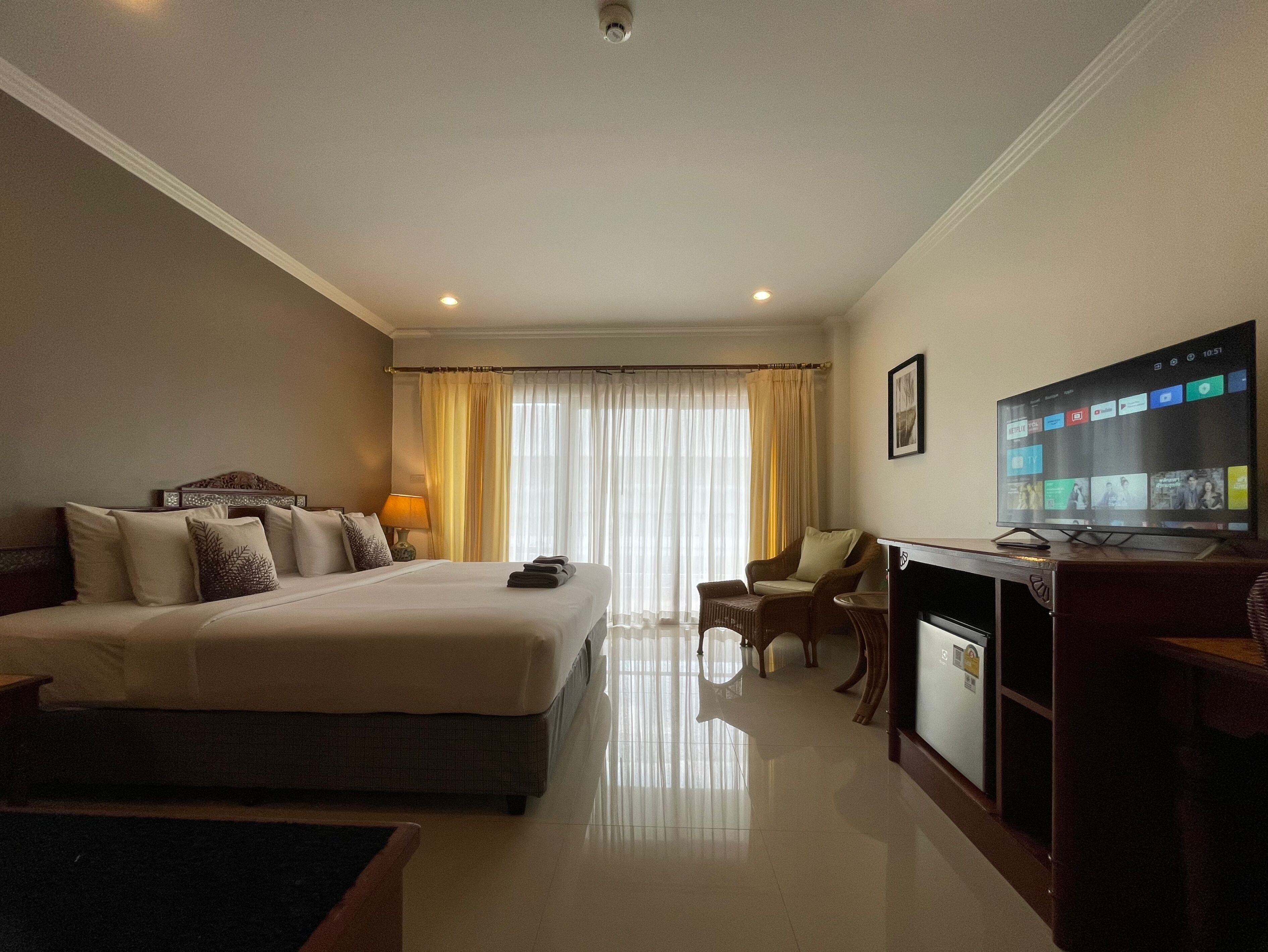 A hotel room with a large bed, a desk with a television, and a chair.