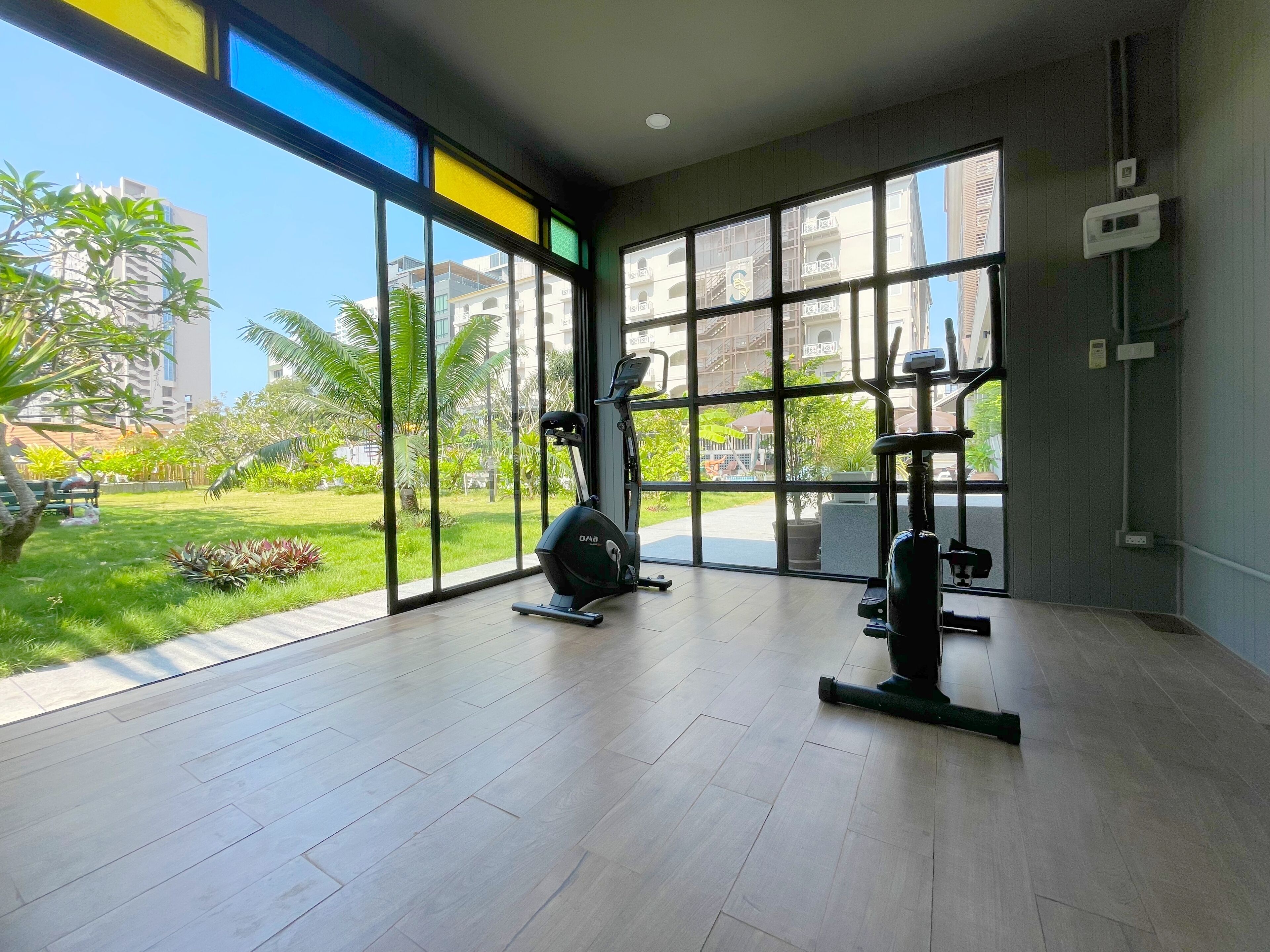 Une salle de sport équipée de matériel d’exercice et dotée de grandes fenêtres donnant sur un espace extérieur verdoyant.