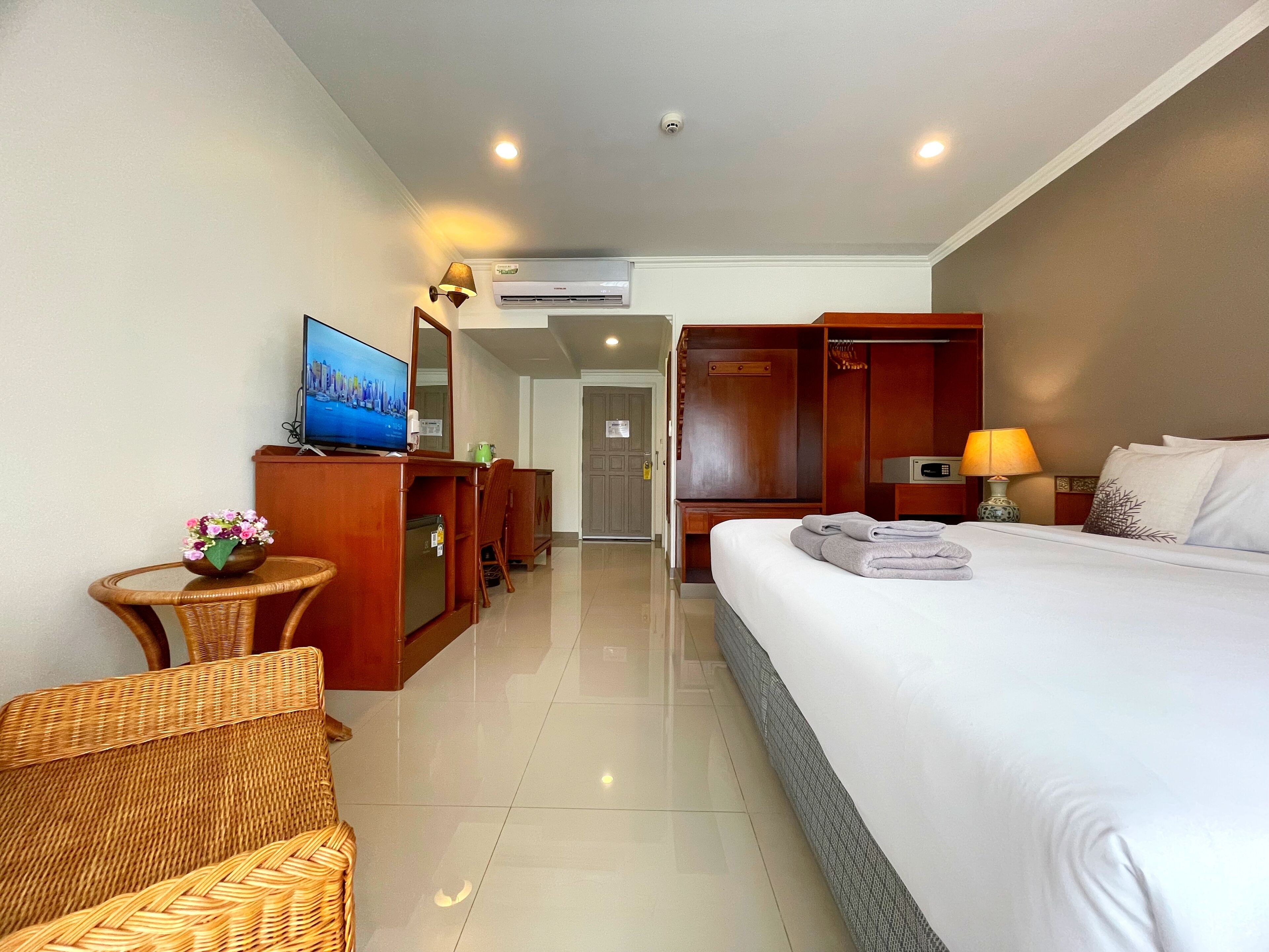 A hotel room with a bed, a television, a desk with a chair, a wardrobe, and a bathroom visible through an open door.