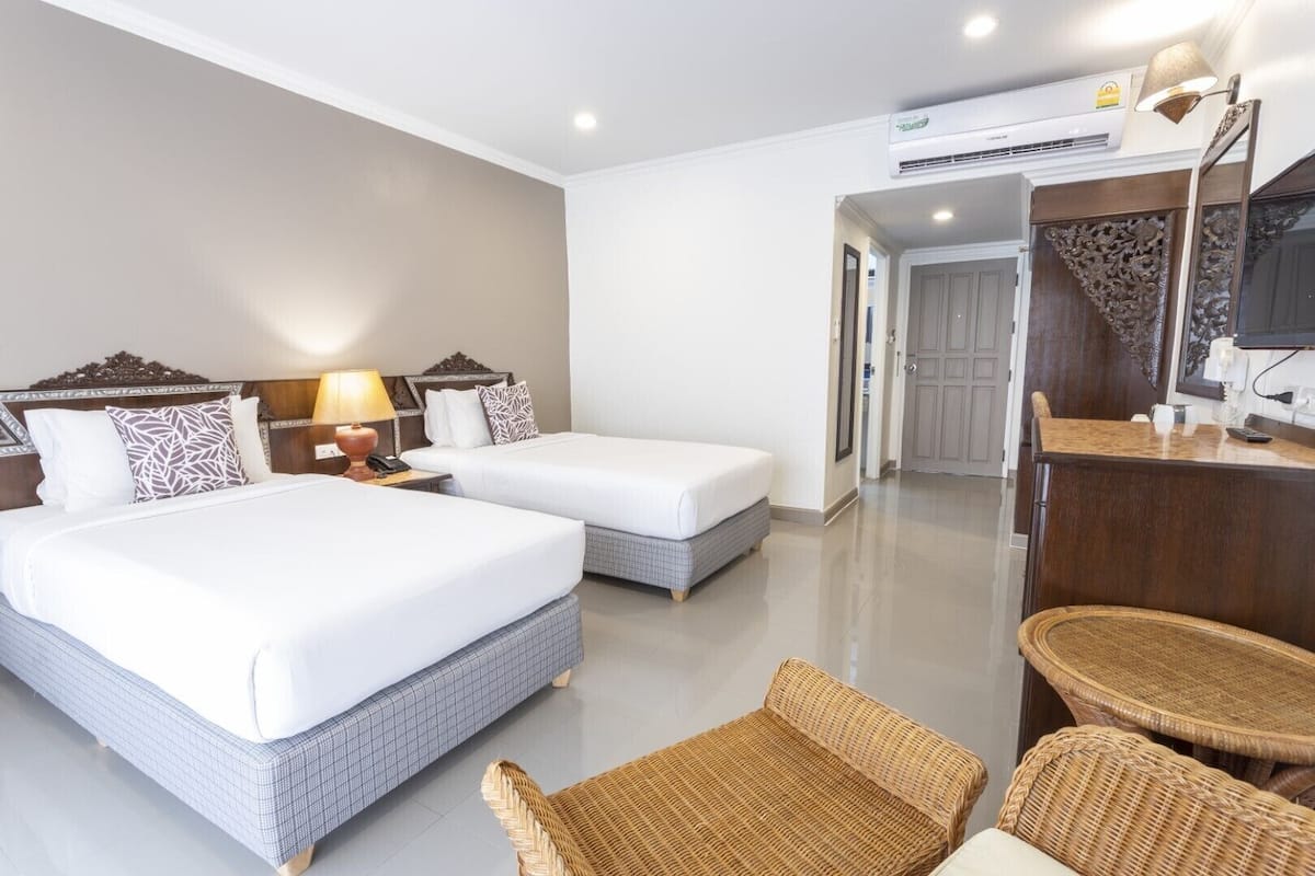 A hotel room with two beds, a small table, wicker chairs, and a TV.