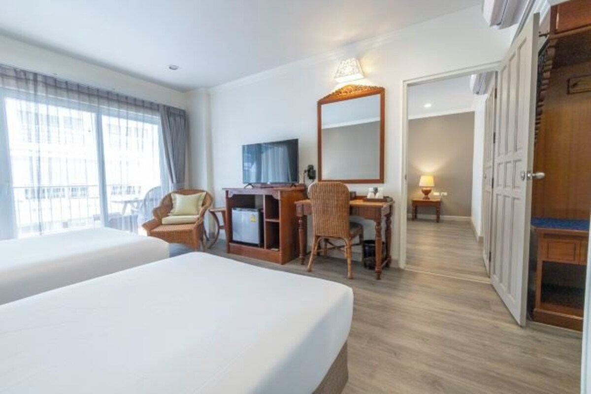 A hotel room with two beds, a desk with a chair, a television, and a mirror.