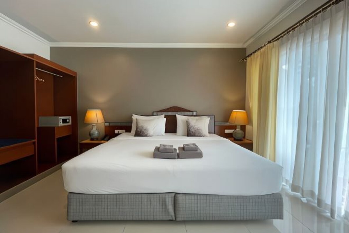 A hotel room with a large bed, two bedside tables with lamps, a wardrobe, and a window with curtains.
