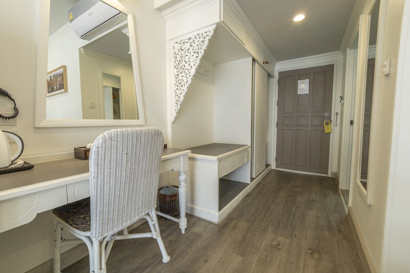 A room with a white desk, a wicker chair, a mirror, and a door with a lock.