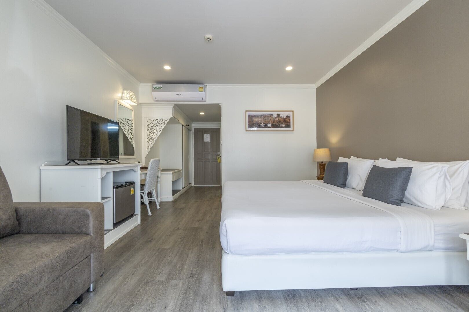 A hotel room with a bed, a desk with a TV, a chair, and a lamp.
