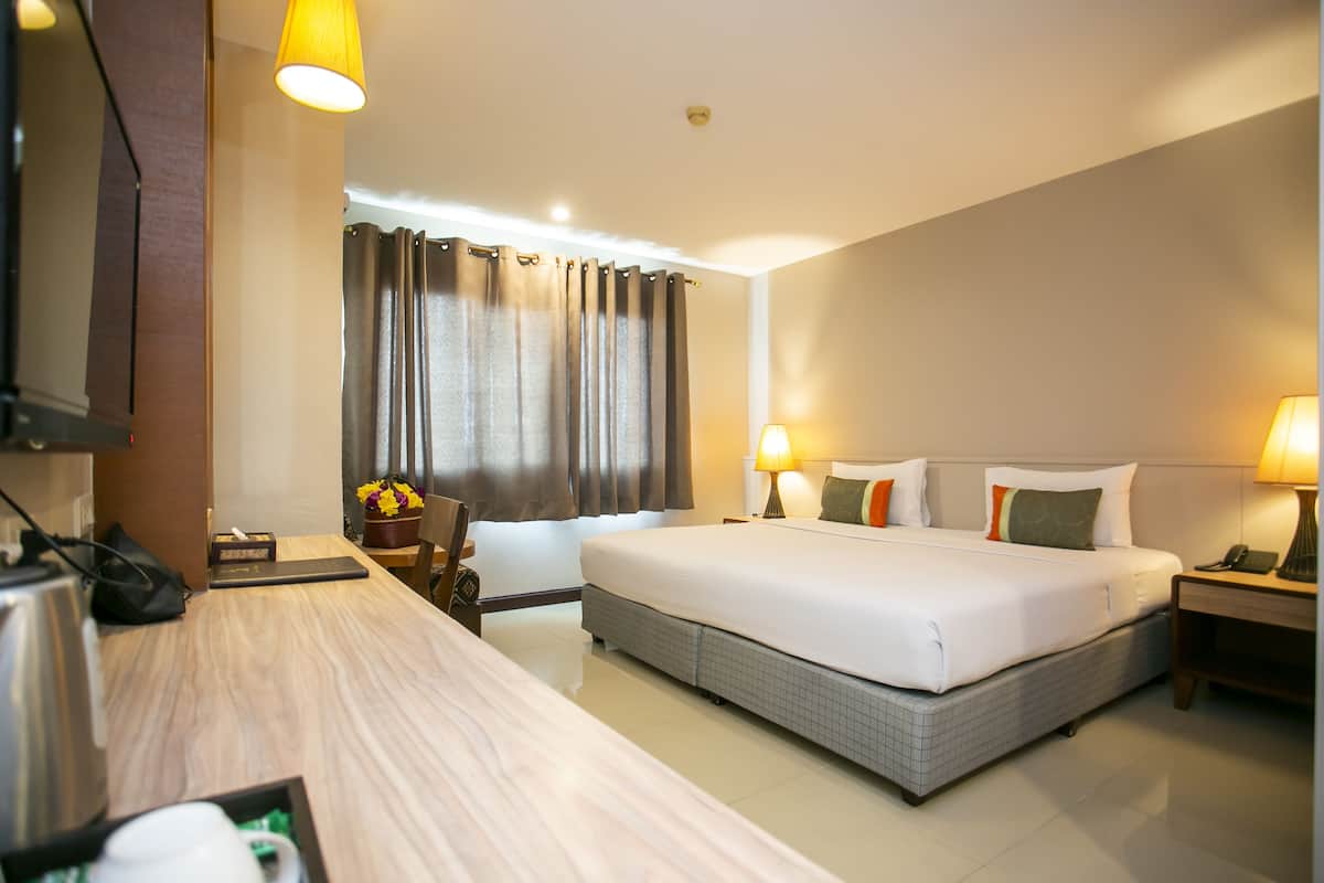 A hotel room with a large bed, bedside tables with lamps, a desk with a kettle, and a window with curtains.