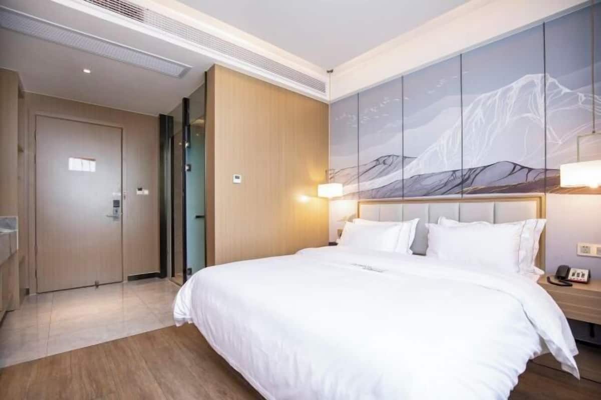 A hotel room with a bed, a nightstand, a wall-mounted lamp, and a door.