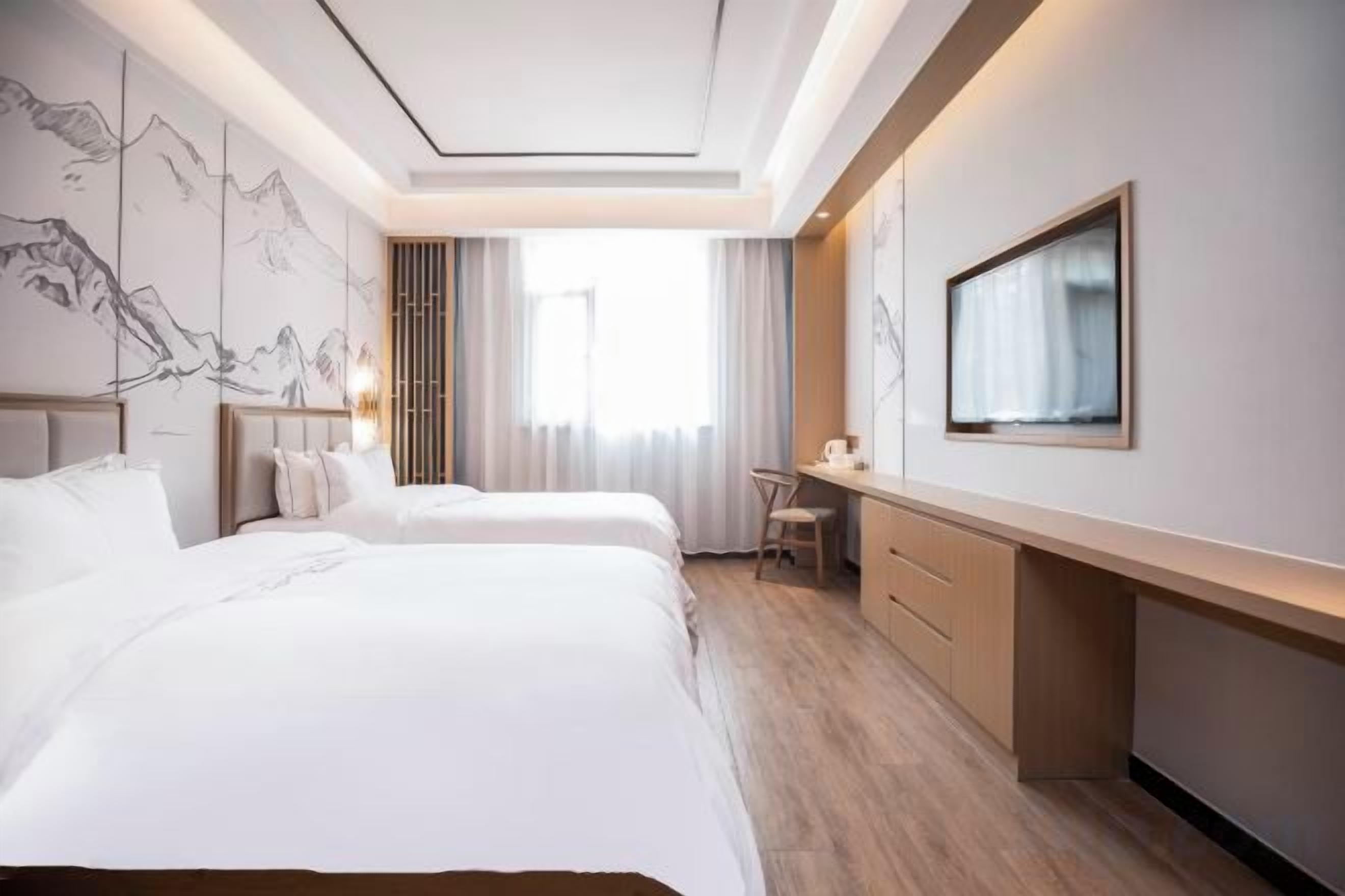 A hotel room with two beds, a desk, and a large window.