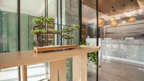 A reception desk with a wooden finish, a bonsai tree display, and modern pendant lighting. - Qingmu Select Hotel (Liyang Tianmu Lake Scenic Area) (Liyang)