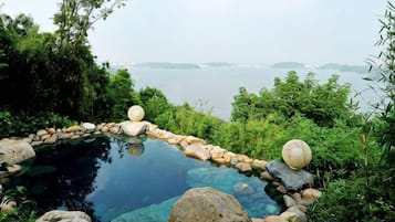 A tranquil outdoor hot spring surrounded by rocks and greenery, overlooking a body of water.