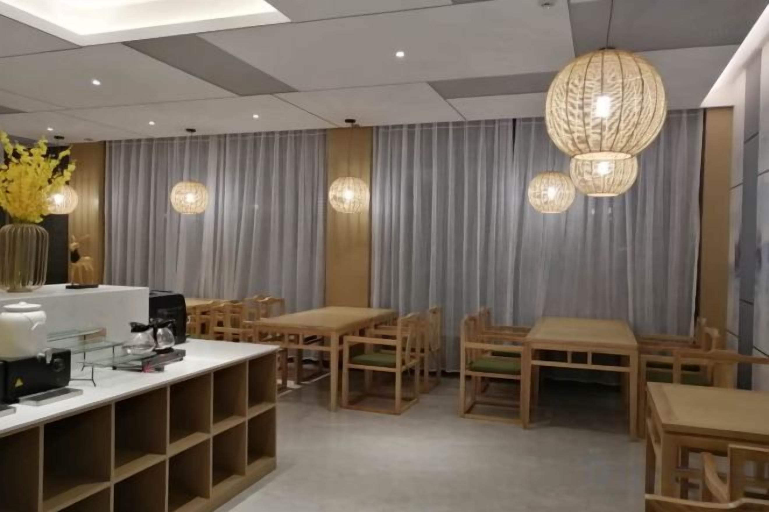A modern dining area with wooden tables and chairs, a white counter with a coffee machine, and decorative hanging lights.