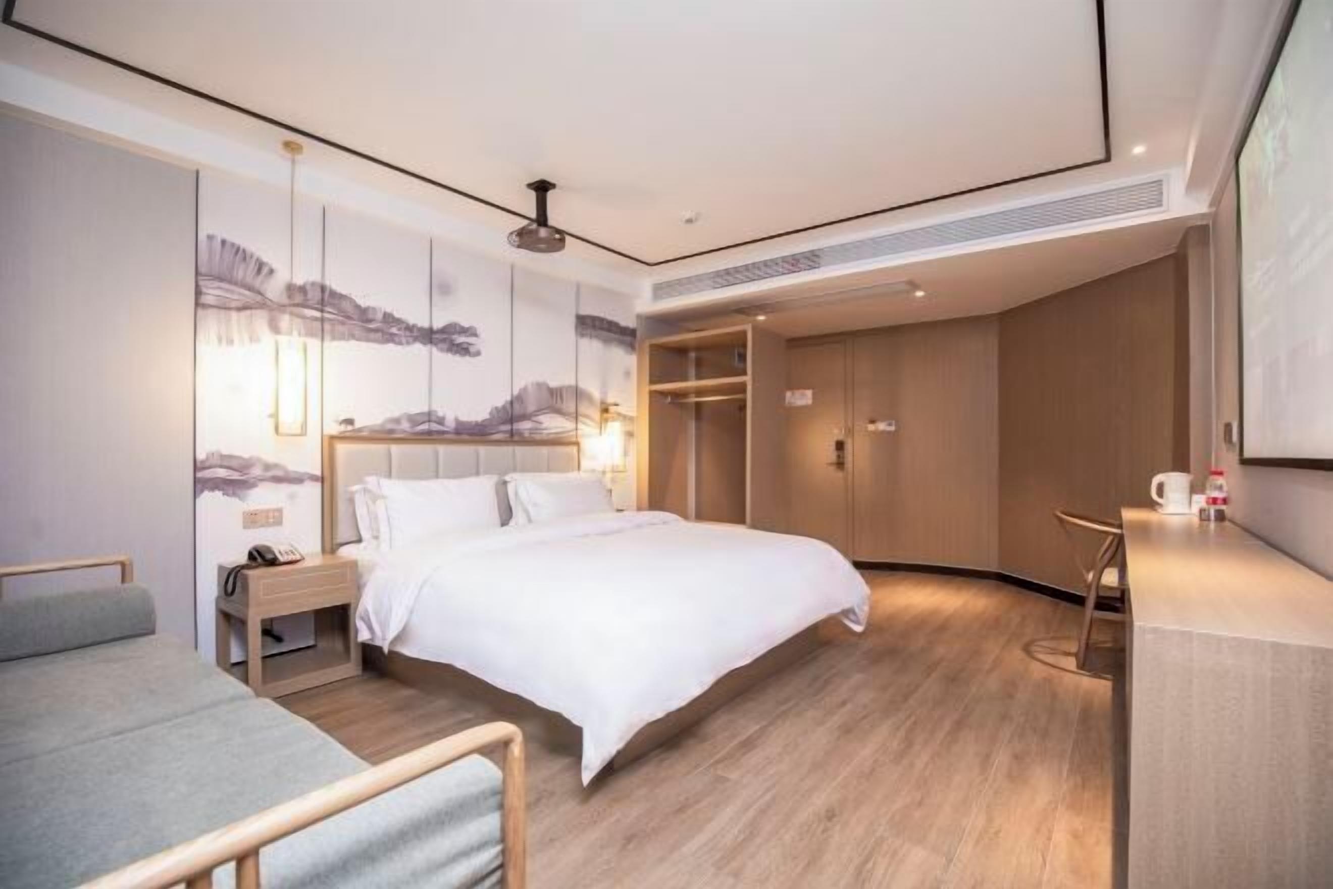 A modern hotel room with a large bed, bedside tables, a desk, and a wardrobe.