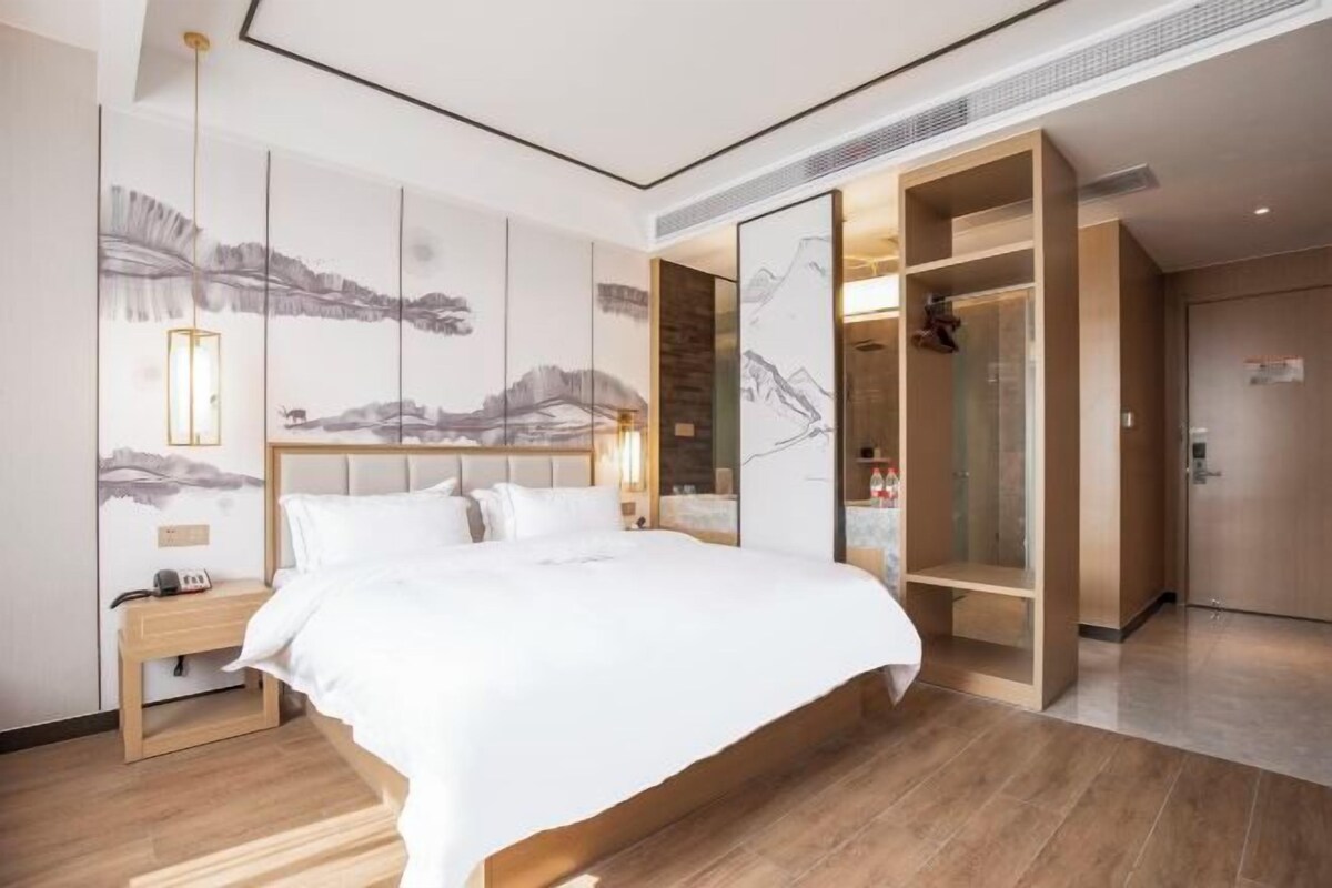 A modern hotel room with a large bed, a wooden nightstand, a wardrobe, and a wall with abstract art.