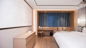 A hotel room with a bed, a desk, a chair, and a large screen on the wall. - Qingmu Select Hotel (Liyang Tianmu Lake Scenic Area) (Liyang)