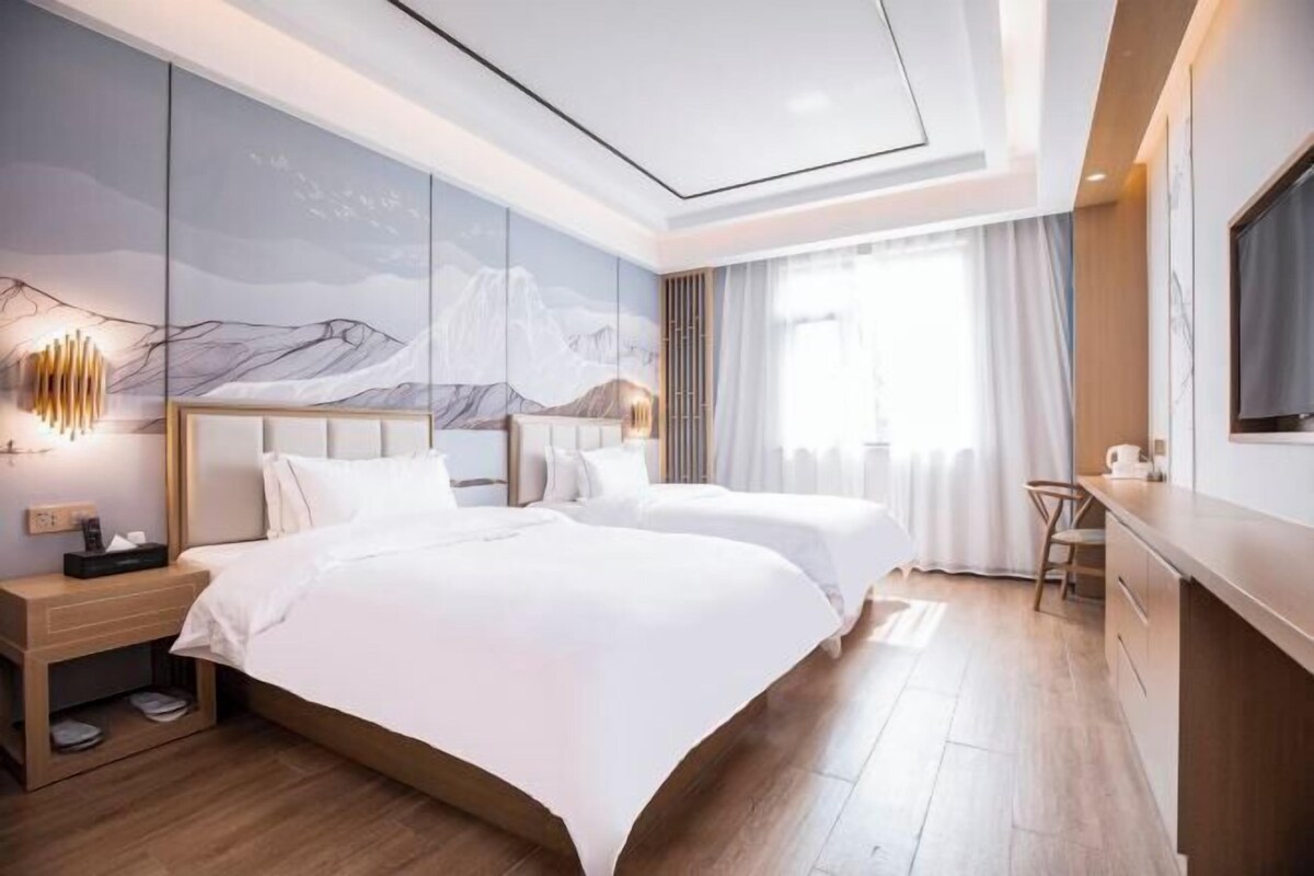 A modern hotel room with two beds, a desk, and a large window.
