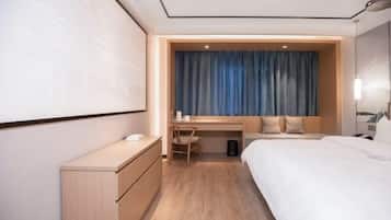 A hotel room with a bed, a desk, a chair, a wardrobe, and a large screen.
