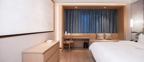 A hotel room with a bed, a desk, a chair, a wardrobe, and a large screen.