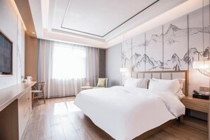 A modern hotel room with a large bed, a desk, a chair, a nightstand, and a wall with a mountain painting. - Qingmu Select Hotel (Liyang Tianmu Lake Scenic Area) (Liyang)