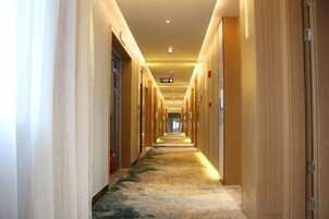 Un largo y estrecho pasillo de hotel con puertas a ambos lados, suelo alfombrado e iluminación empotrada en el techo.