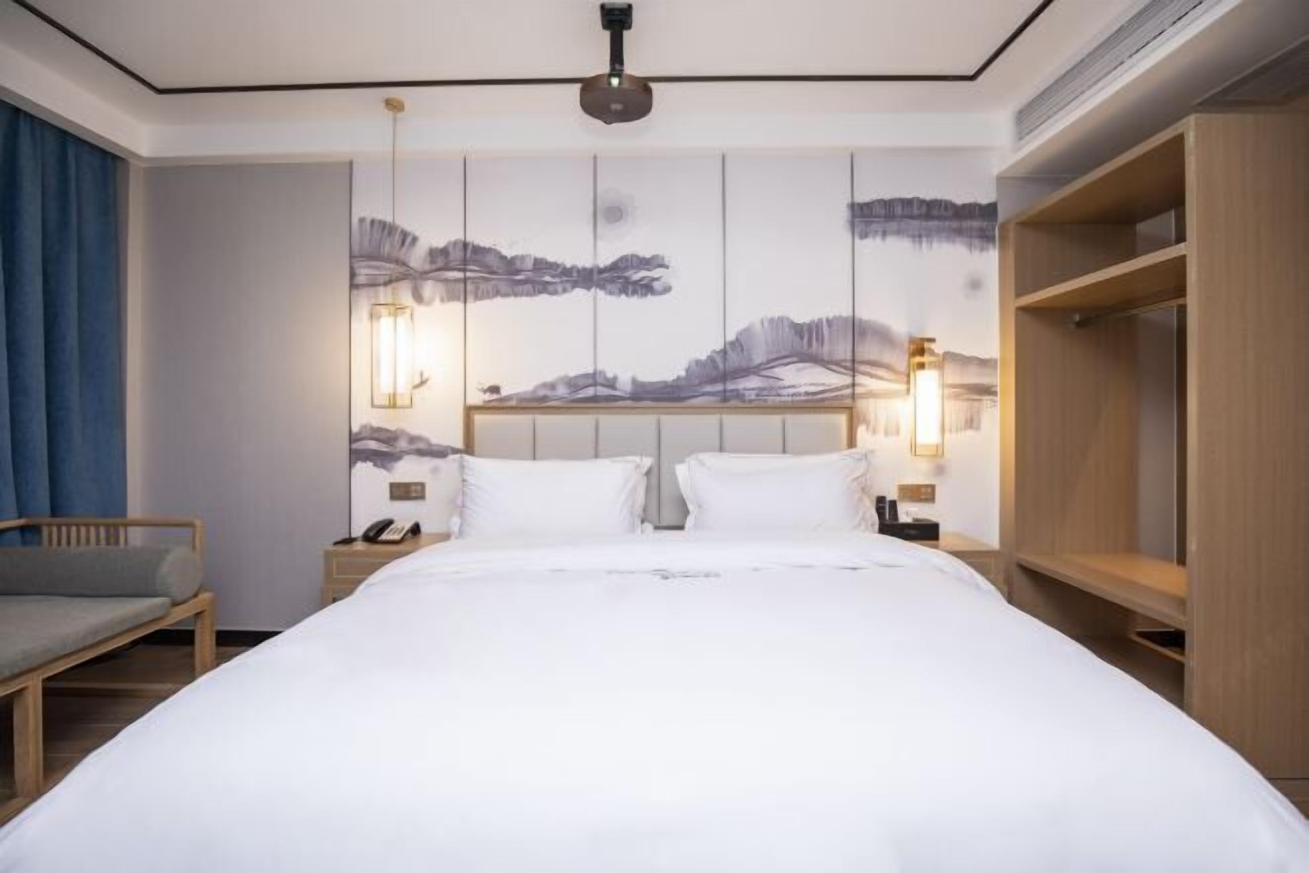 A hotel room with a large bed, bedside tables, a nightstand, a chair, and a wardrobe.
