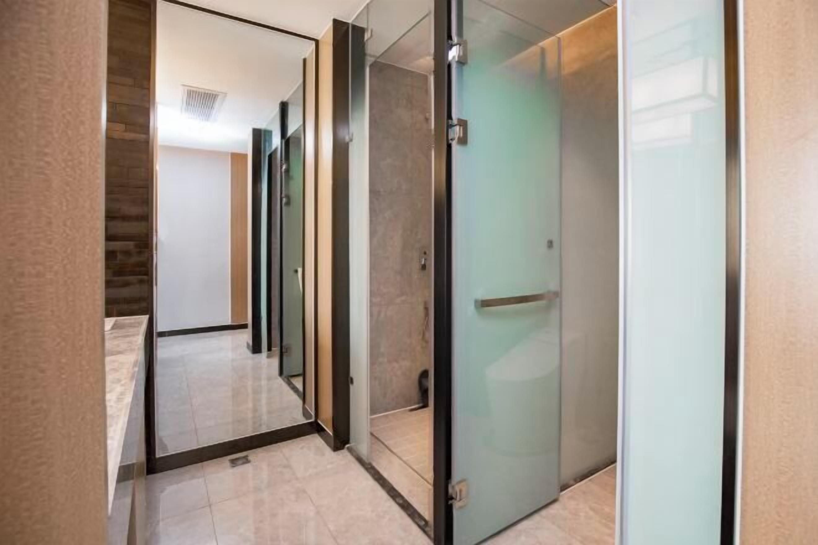 Un pasillo con puertas de vidrio, piso de baldosas y una escalera visible al fondo.