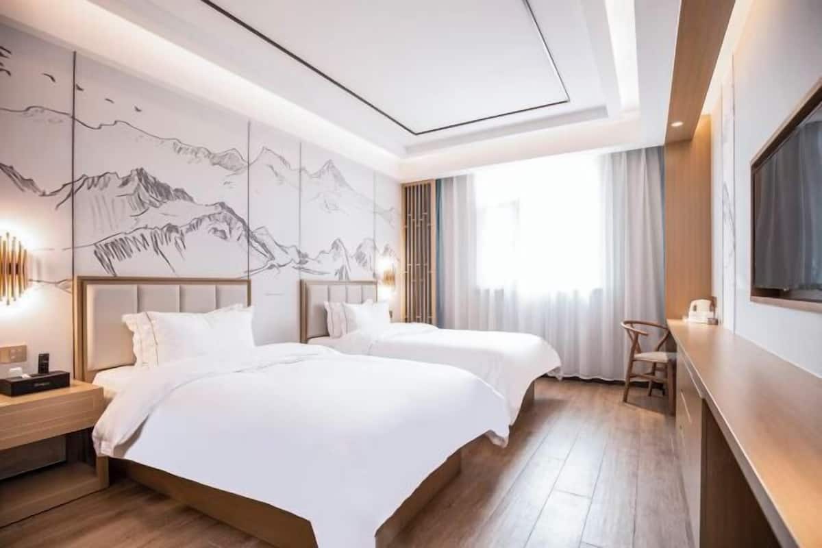 A hotel room with two beds, a large wall mural, a TV, and a wooden floor.
