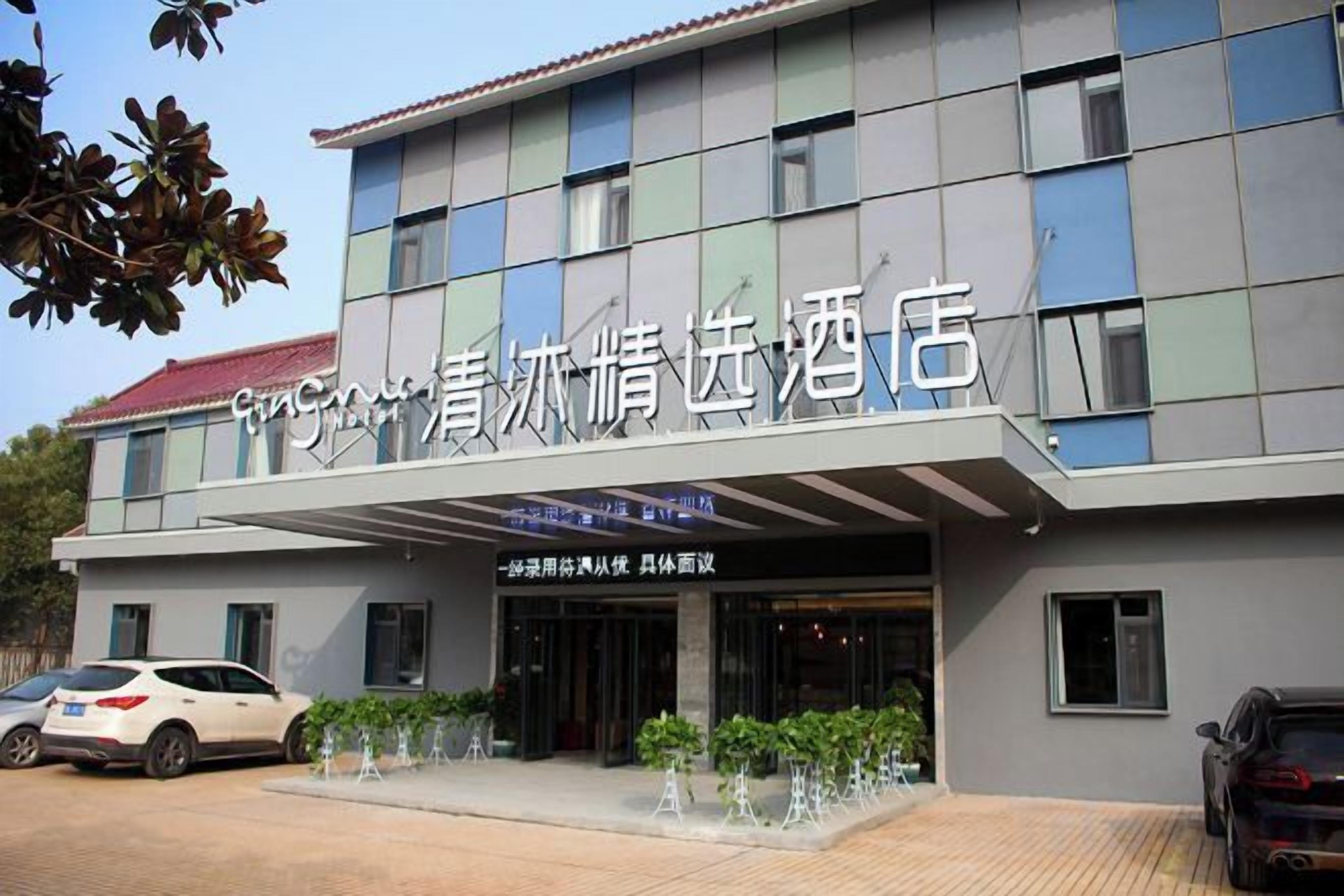 A hotel with a modern facade, a covered entrance, and a parking area with cars.