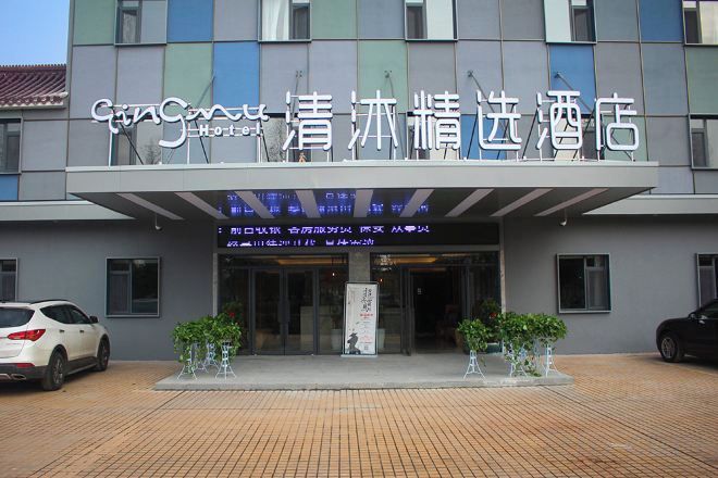 A hotel entrance with a sign in a foreign language, a covered walkway, and two potted plants.