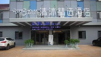 A hotel entrance with a sign in a foreign language, a covered walkway, and two potted plants.
