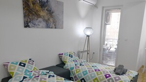 Makuuhuoneessa on kaksi sänkyä, suuri abstrakti maalaus, lattiavalaisin ja ikkuna, jossa on sälekaihtimet.