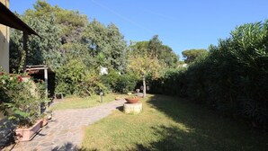 En stenlagd gång leder till en trädgård med olika sorters växter i krukor och en pergola.