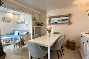 Een moderne woonkamer met een witte tafel, grijze stoelen, een blauwe bank en een open haard.