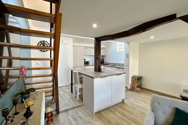 A modern kitchen with a central island, wooden beams, and a dining area with a table and chairs.