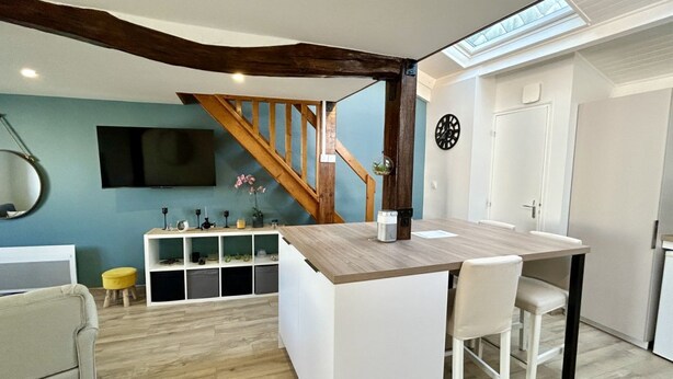 A modern kitchen with a wooden island, white bar stools, a built-in TV, and a staircase with exposed beams.