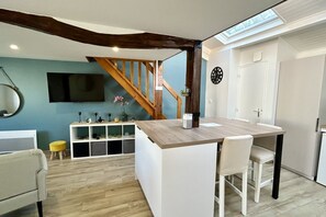 A modern kitchen with a wooden island, white bar stools, a built-in TV, and a staircase with exposed beams.