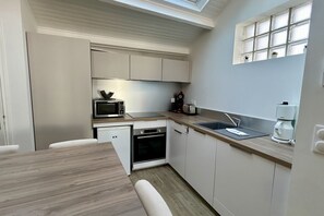 A compact kitchen with a microwave, oven, sink, and a window above the countertop.