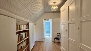 A hallway with wooden flooring, white walls, a bookshelf, a chair, and a door. - Anna & Jules' little house (Saint-Quentin-en-Tourmont)