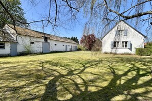 A rural property with a large open grassy area, two white buildings, and trees casting shadows.