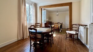 A dining room with a wooden table and chairs, a chandelier, and a view through an open doorway. - Anna & Jules' little house (Saint-Quentin-en-Tourmont)