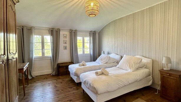 A room with two beds, a wooden floor, a chandelier, and a window with curtains. - Anna & Jules' little house (Saint-Quentin-en-Tourmont)