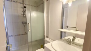 Une salle de bain avec une douche à parois de verre, des toilettes, un lavabo avec un miroir et un pommeau de douche.