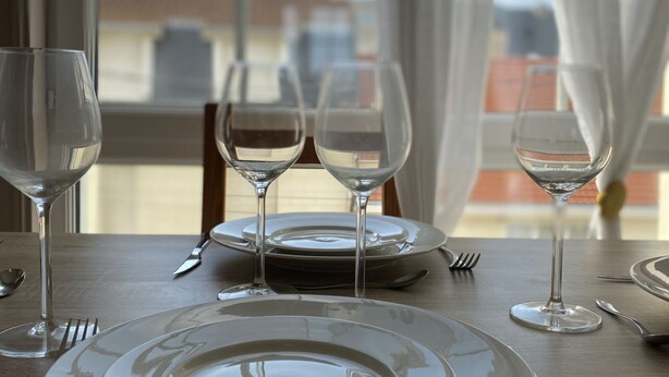 Une table à manger avec quatre verres à vin et des assiettes, placée devant une fenêtre ornée de rideaux.